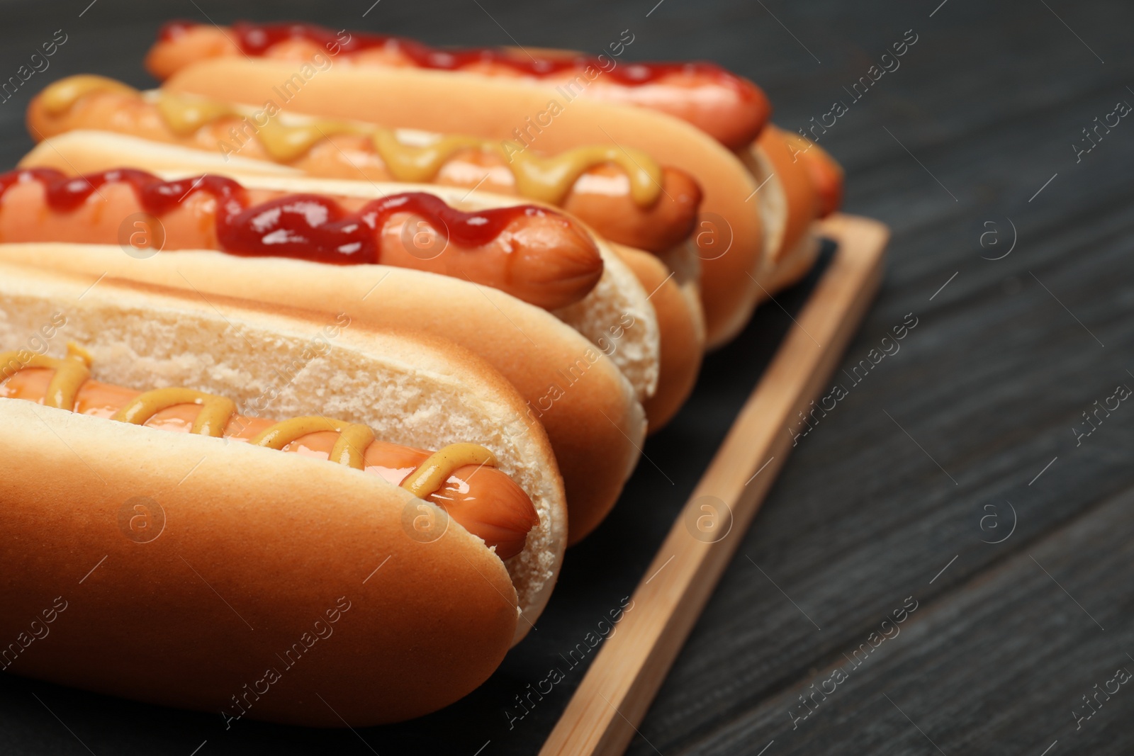 Photo of Board with hot dogs on wooden table, closeup. Space for text