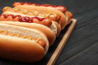 Board with hot dogs on wooden table, closeup. Space for text