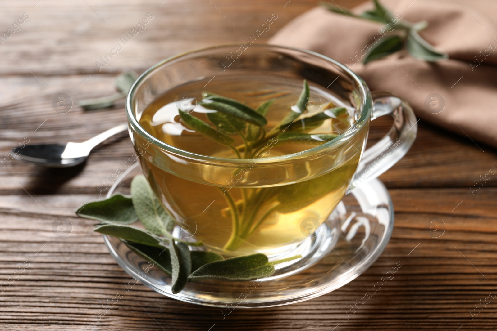 Photo of Cup of aromatic sage tea and fresh leaves on wooden table