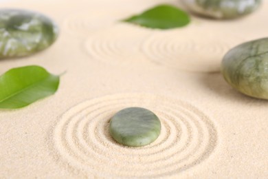 Photo of Zen garden stones and leaves on beige sand with pattern