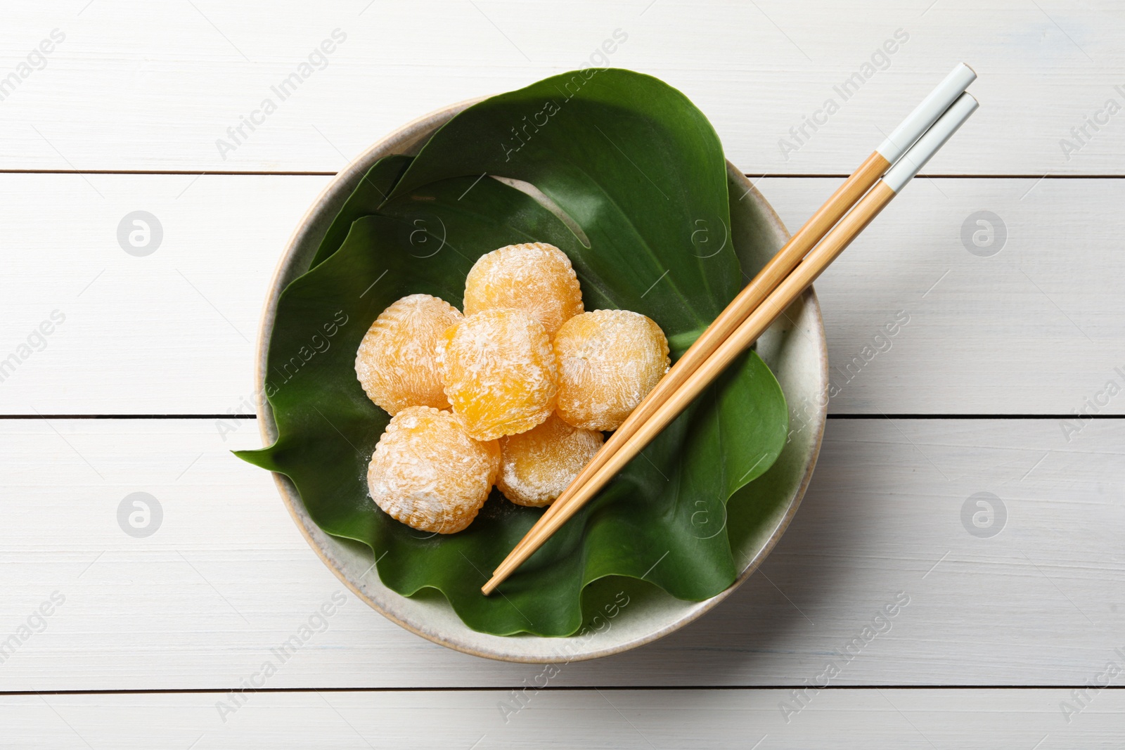 Photo of Delicious mochi served in bowl with green leaf and chopsticks on white wooden table, top view. Traditional Japanese dessert