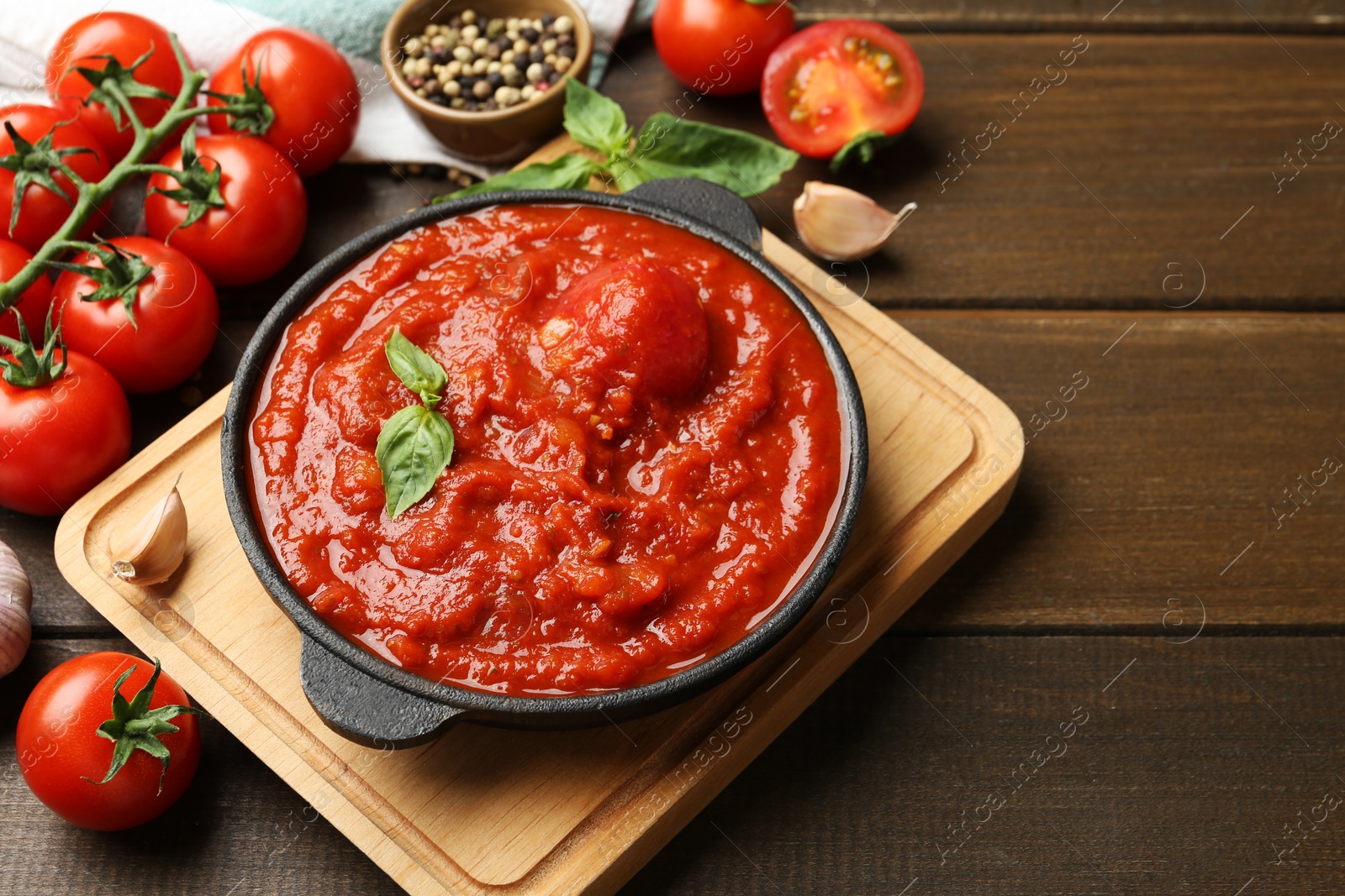 Photo of Homemade tomato sauce in bowl and ingredients on wooden table, space for text