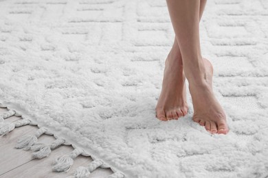 Photo of Woman standing on soft white carpet at home, closeup. Space for text