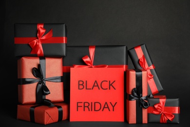 Photo of Many gift boxes and sheet of paper with words Black Friday on dark background