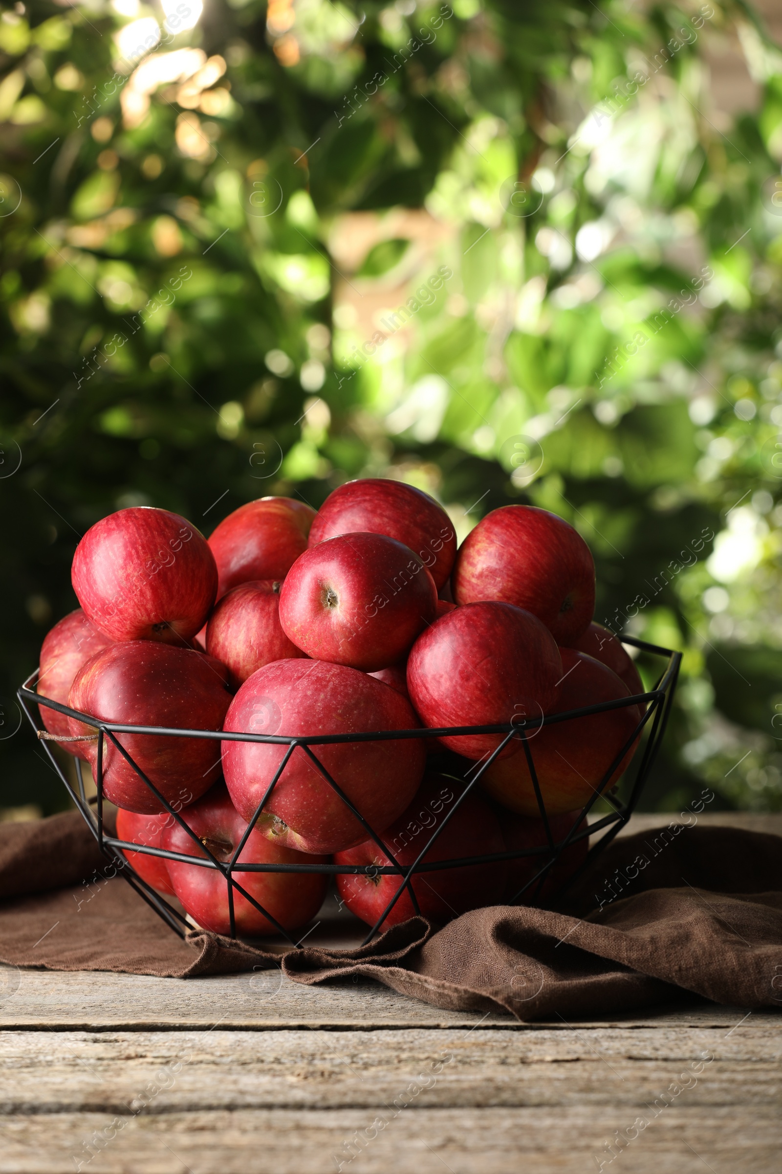 Photo of Ripe red apples in bowl on wooden table outdoors