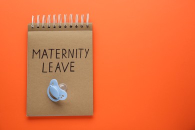 Photo of Notepad with words Maternity Leave and baby pacifier on orange background, top view. Space for text
