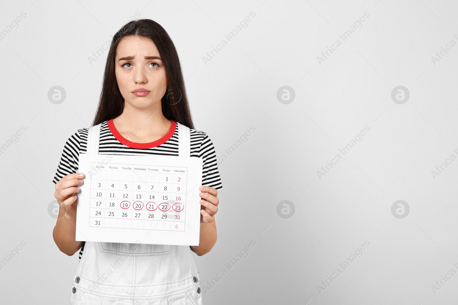 Photo of Young woman holding calendar with marked menstrual cycle days on light background. Space for text