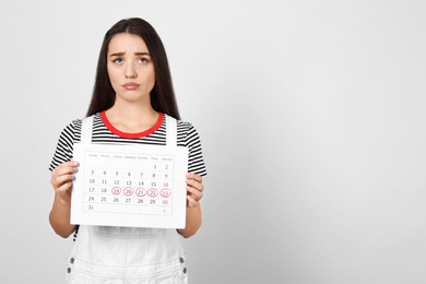 Young woman holding calendar with marked menstrual cycle days on light background. Space for text