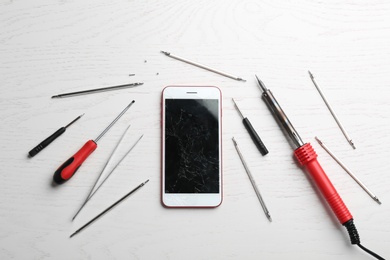 Photo of Mobile phone with broken display and repair tools on wooden table, flat lay