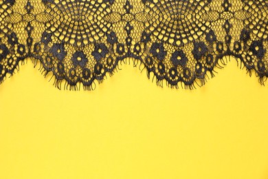 Photo of Black lace on yellow background, top view. Space for text