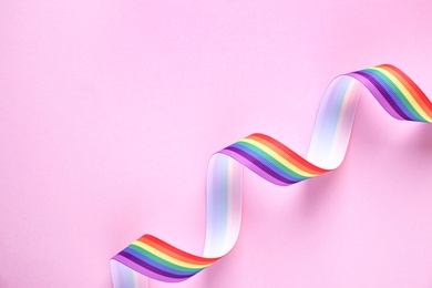 Photo of Top view of rainbow ribbon on pink background, space for text. Gay symbol