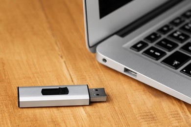 Photo of Modern laptop and usb flash drive on wooden table, closeup