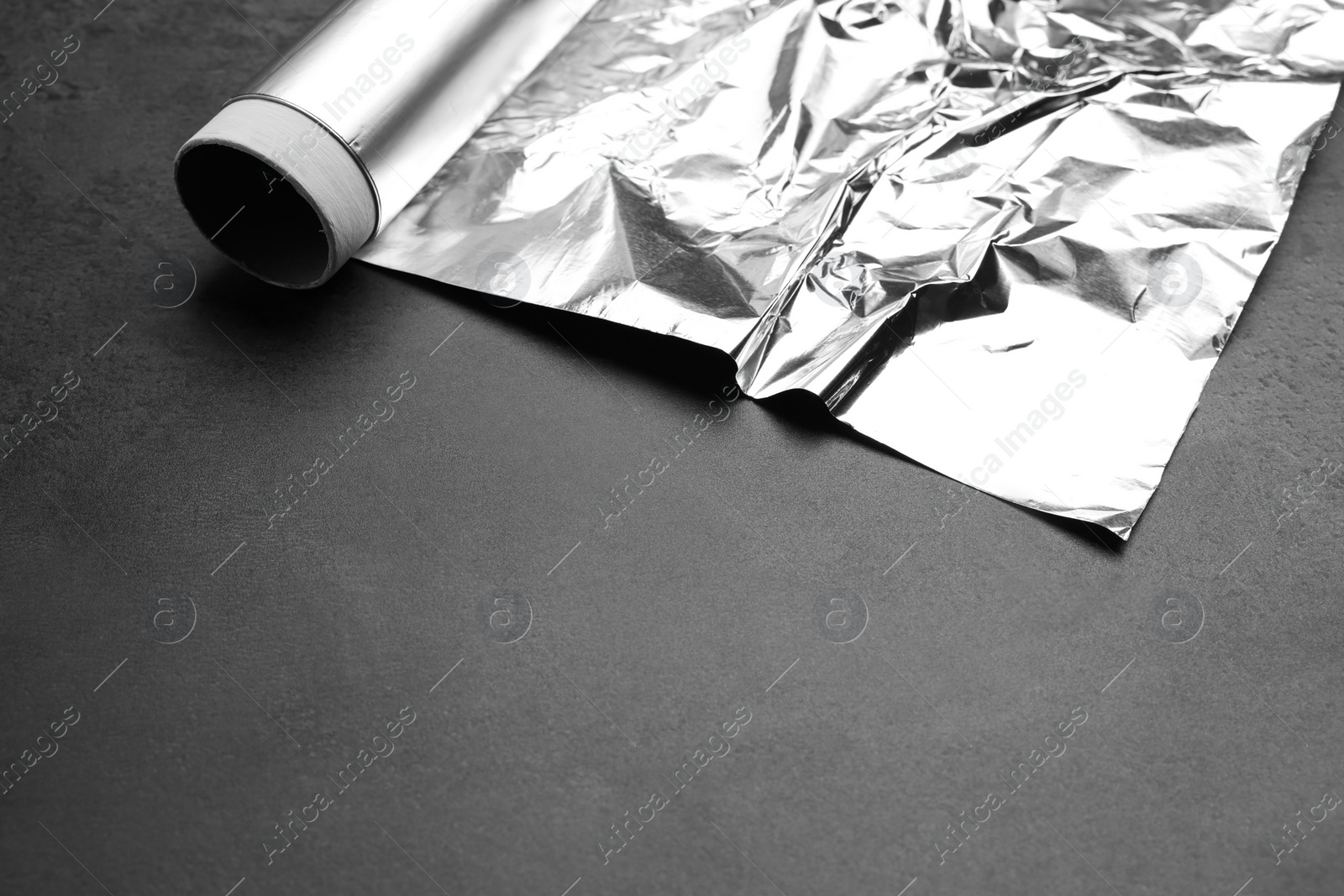 Photo of Roll of aluminum foil on grey dark table, closeup. Space for text