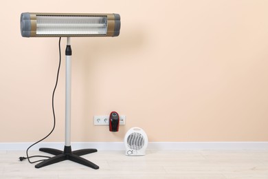 Different electric heaters near beige wall indoors, space for text