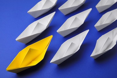 Photo of Yellow paper boat leading others on blue background, above view. Leadership concept
