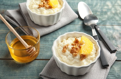 Photo of Creamy rice pudding with walnuts and orange slices in ramekins served on wooden table