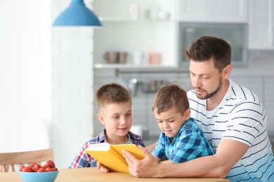 Photo of Dad and his sons reading interesting book in kitchen. Space for text