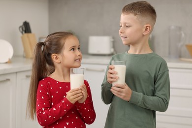 Cute children with glasses of fresh milk in kitchen