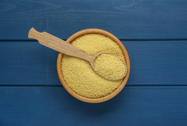 Bowl and spoon with raw couscous on blue wooden table, top view