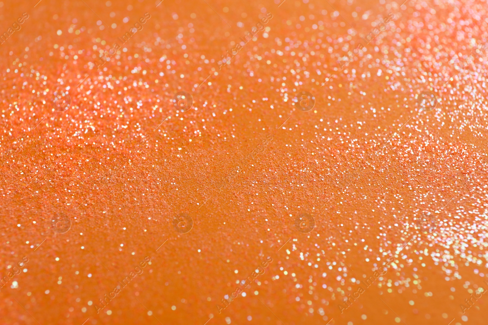 Photo of Shiny bright glitter on orange background, closeup