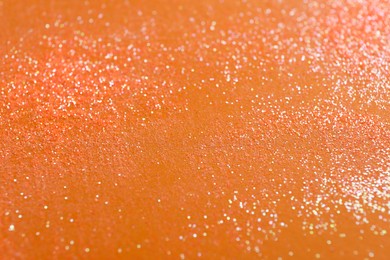 Photo of Shiny bright glitter on orange background, closeup