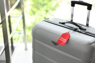 Photo of Stylish suitcase with travel insurance label on blurred background, closeup. Space for text
