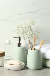 Photo of Different bath accessories, personal care products and gypsophila flowers in vase on gray table near white marble wall