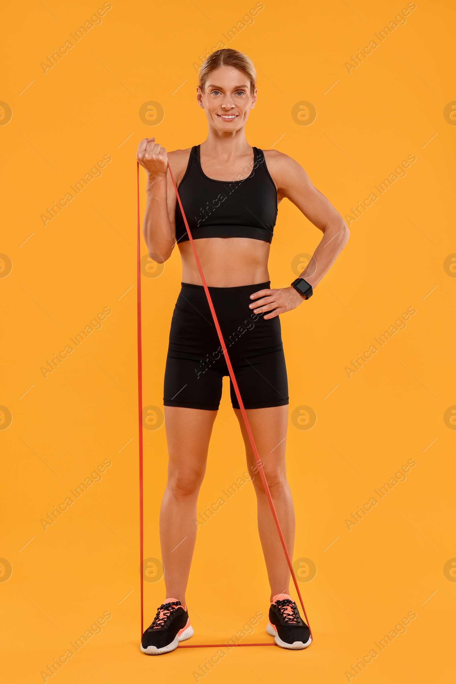 Photo of Woman exercising with elastic resistance band on orange background