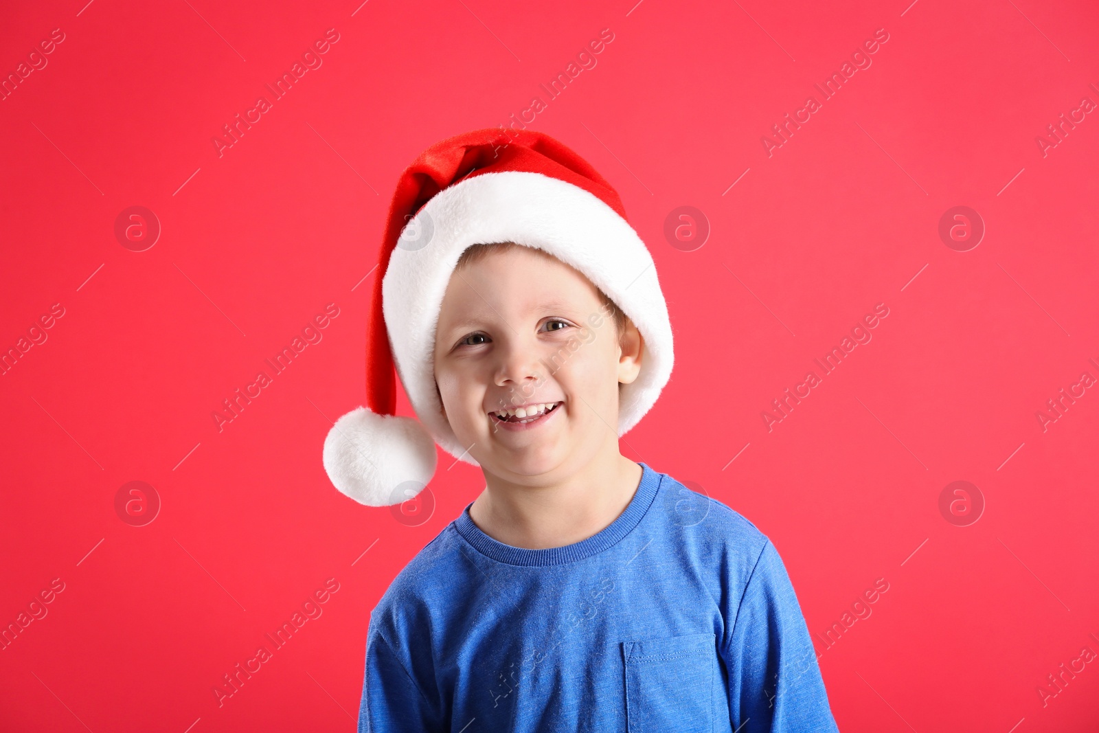 Photo of Cute little boy wearing Santa Claus hat on red background