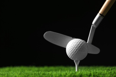 Photo of Hitting golf ball with club on artificial grass against black background, space for text