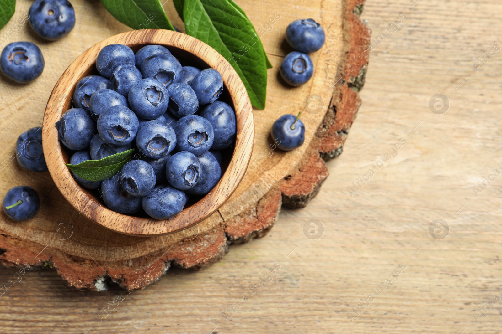 Photo of Bowl of tasty fresh blueberries with leaves on wooden table, flat lay. Space for text