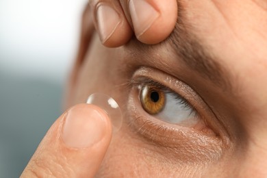 Photo of Man putting contact lens in his eye on blurred background, closeup