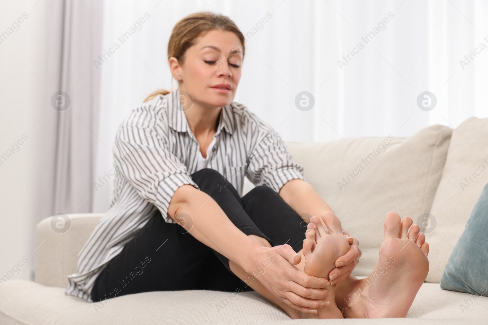 Photo of Woman suffering from foot pain on sofa indoors. Arthritis symptoms