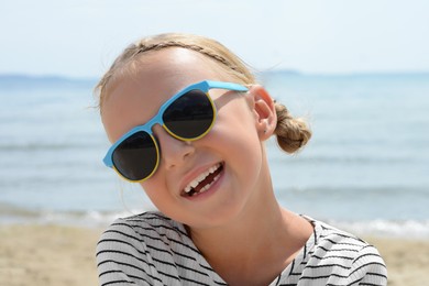 Little girl wearing sunglasses at beach on sunny day