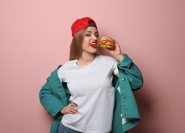 Pretty woman eating tasty burger on color background