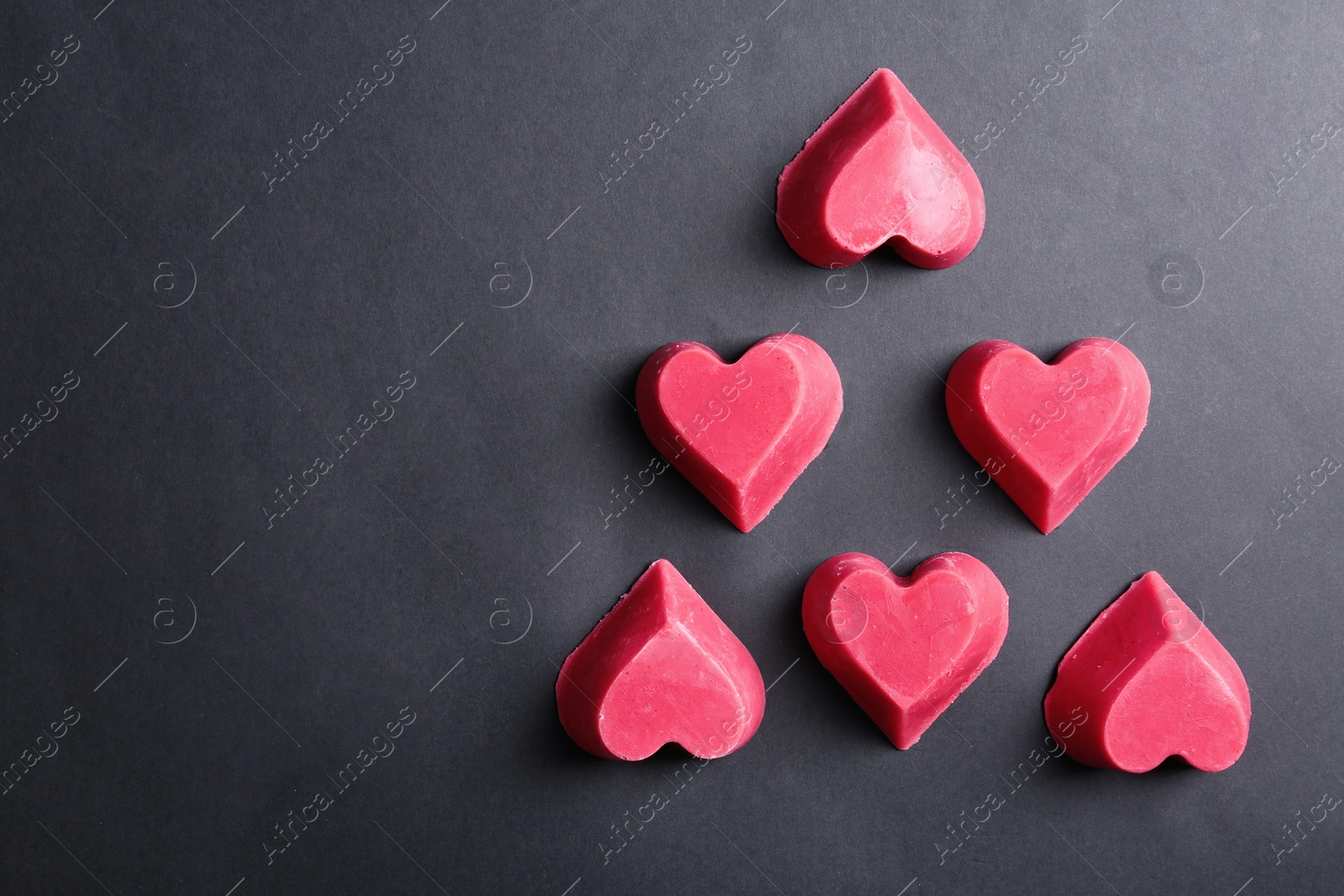 Photo of Heart shaped berry ice cubes on black background, flat lay. Space for text