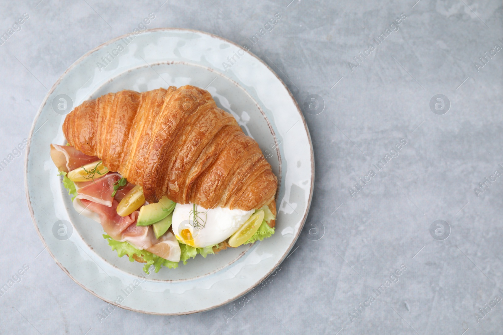 Photo of Delicious croissant with prosciutto, avocado and egg on grey table, top view. Space for text