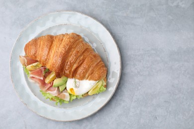 Photo of Delicious croissant with prosciutto, avocado and egg on grey table, top view. Space for text