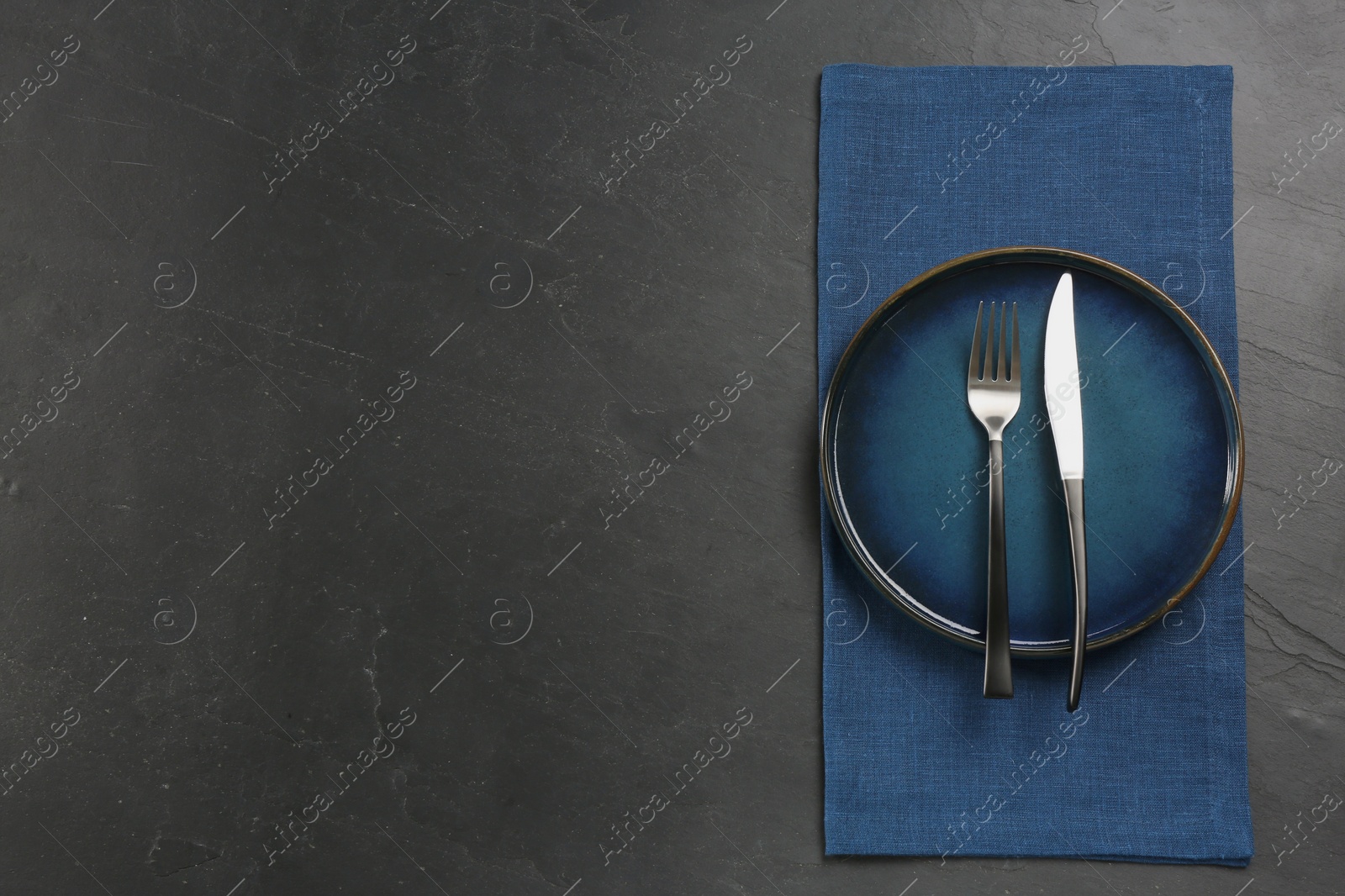 Photo of Ceramic plate, fork and knife on black table, top view. Space for text