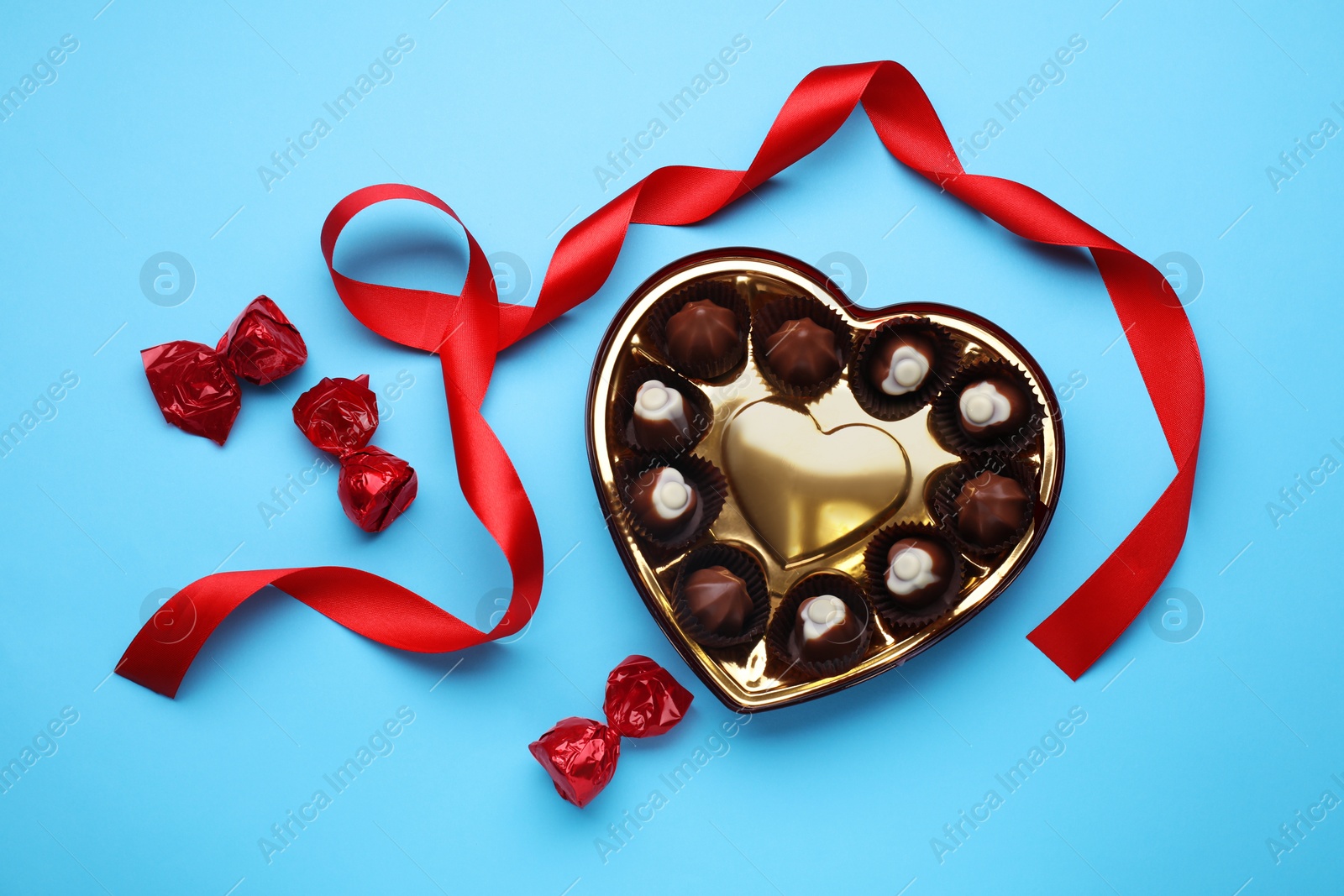 Photo of Heart shaped box with delicious chocolate candies and ribbon on light blue background, flat lay