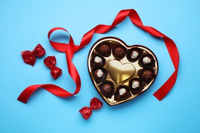Heart shaped box with delicious chocolate candies and ribbon on light blue background, flat lay