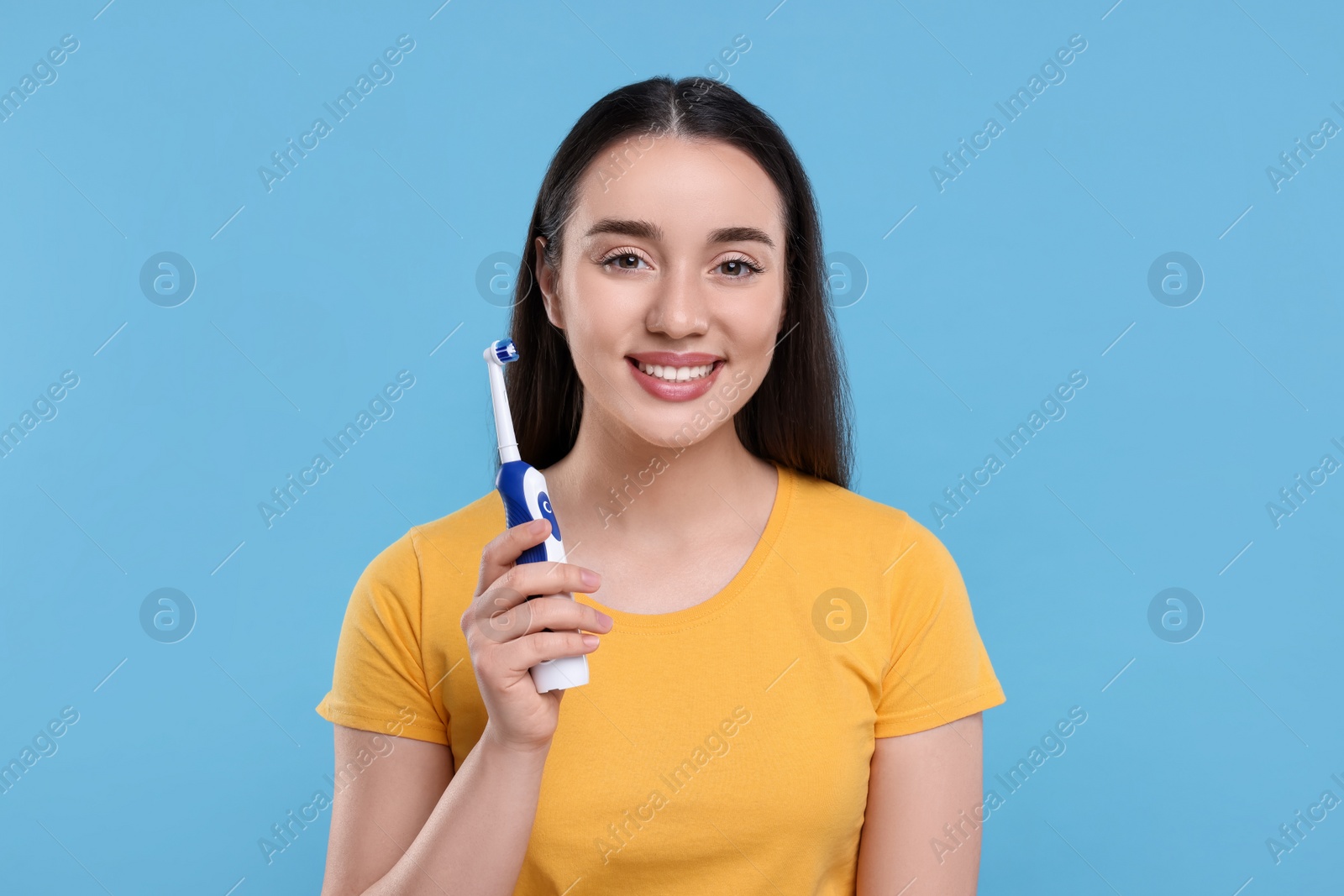Photo of Happy young woman holding electric toothbrush on light blue background