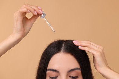 Woman applying hair serum on beige background, closeup. Cosmetic product