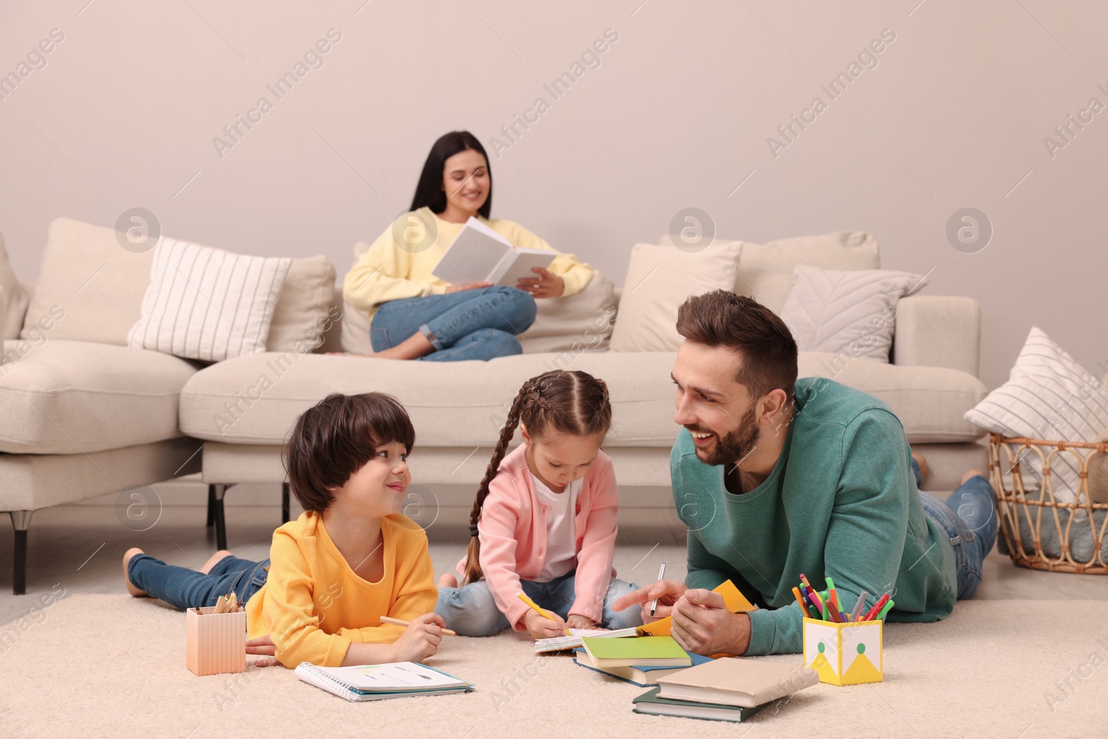 Photo of Father playing with his children while mother reading book on sofa in living room