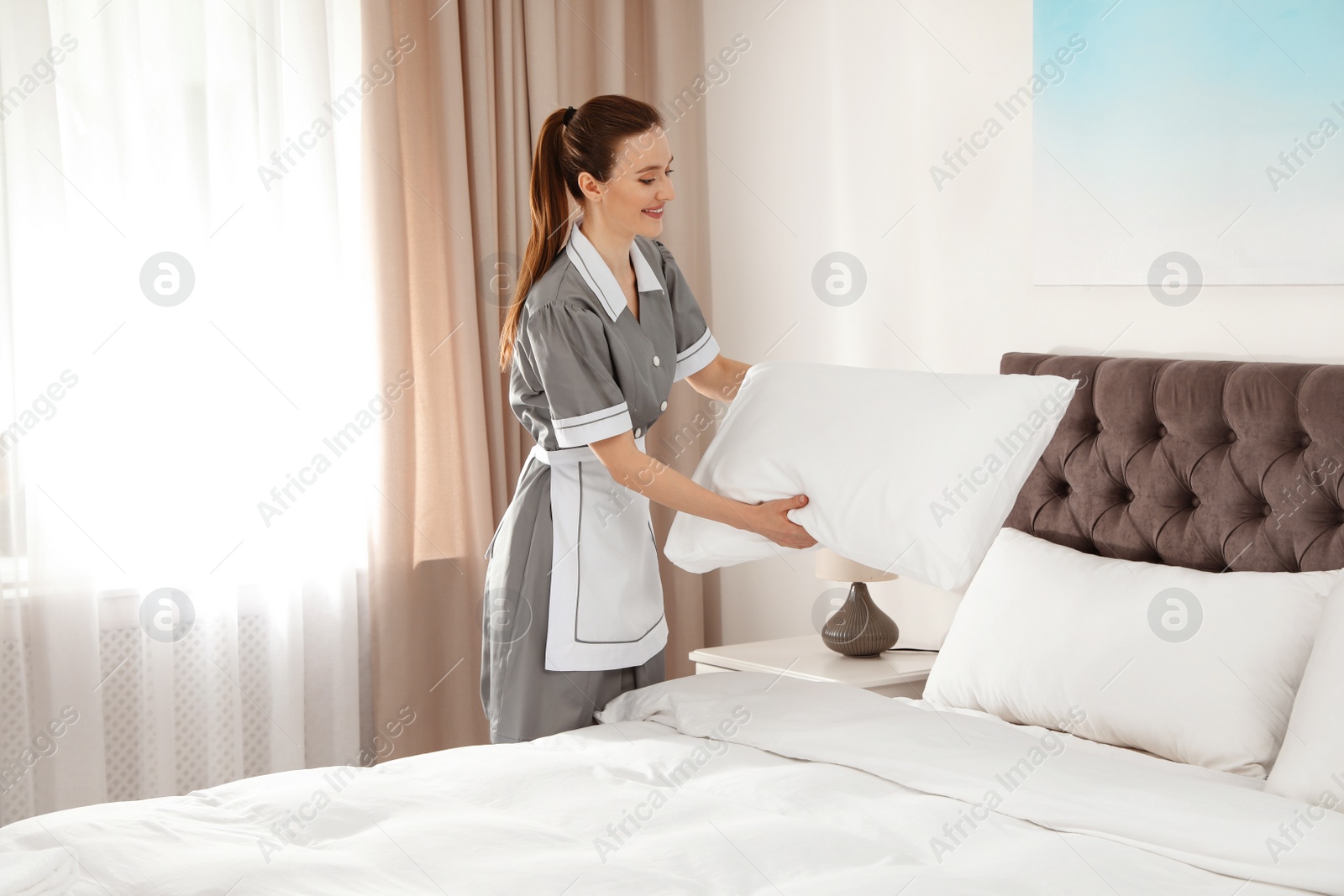 Photo of Young chambermaid making bed in hotel room