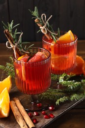 Photo of Christmas Sangria cocktail in glasses, ingredients and fir tree branches on wooden table, closeup