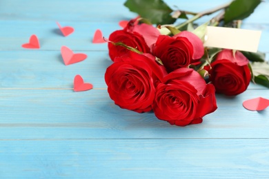 Photo of Beautiful red roses and paper hearts on light blue wooden table. Valentine's Day celebration