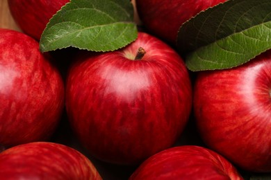 Photo of Ripe red apples and green leaves as background, closeup