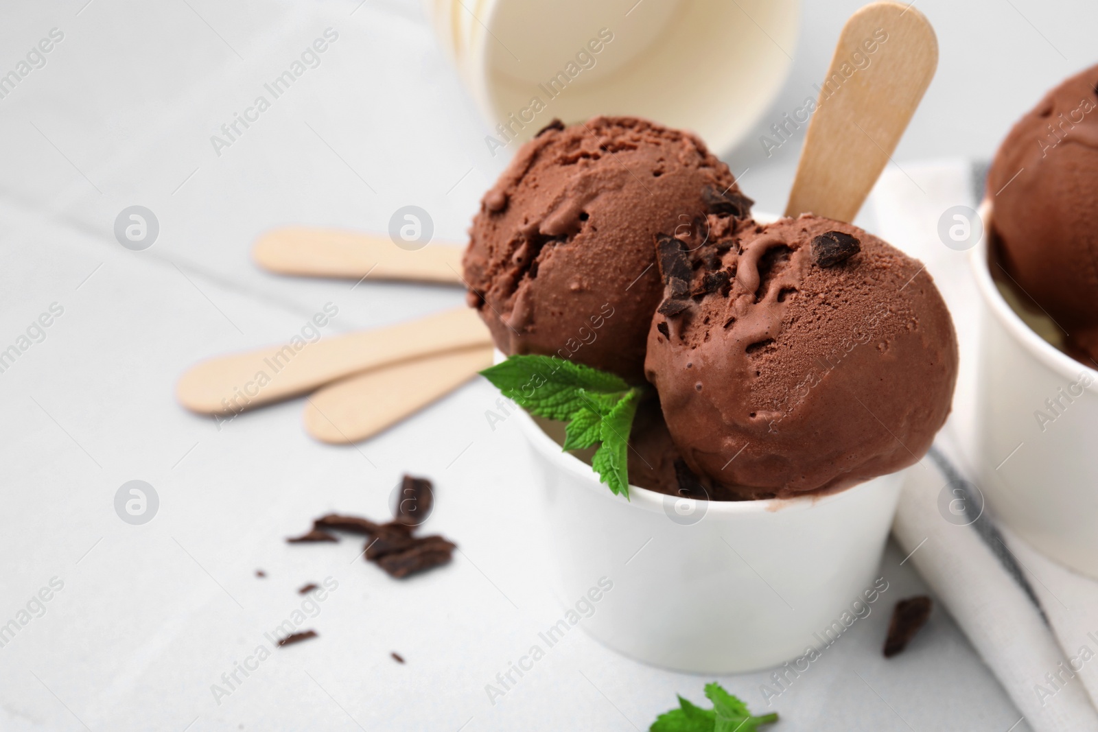 Photo of Paper cups with tasty chocolate ice cream on white tiled table, closeup. Space for text