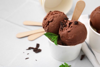 Photo of Paper cups with tasty chocolate ice cream on white tiled table, closeup. Space for text